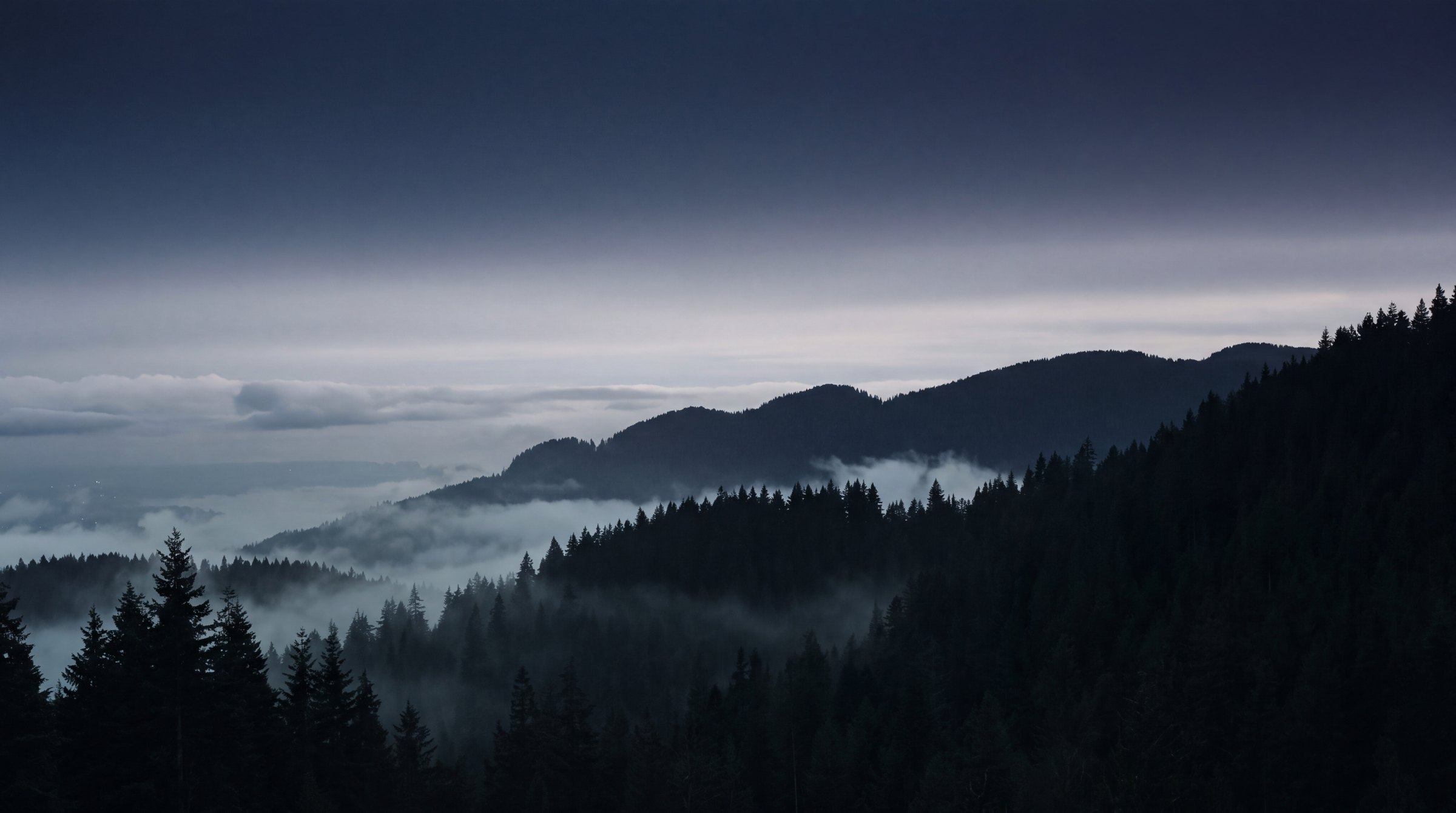 Layered ridgelines of the North Shore mountains above Vancouver at dusk, low cloud held in the valleys
